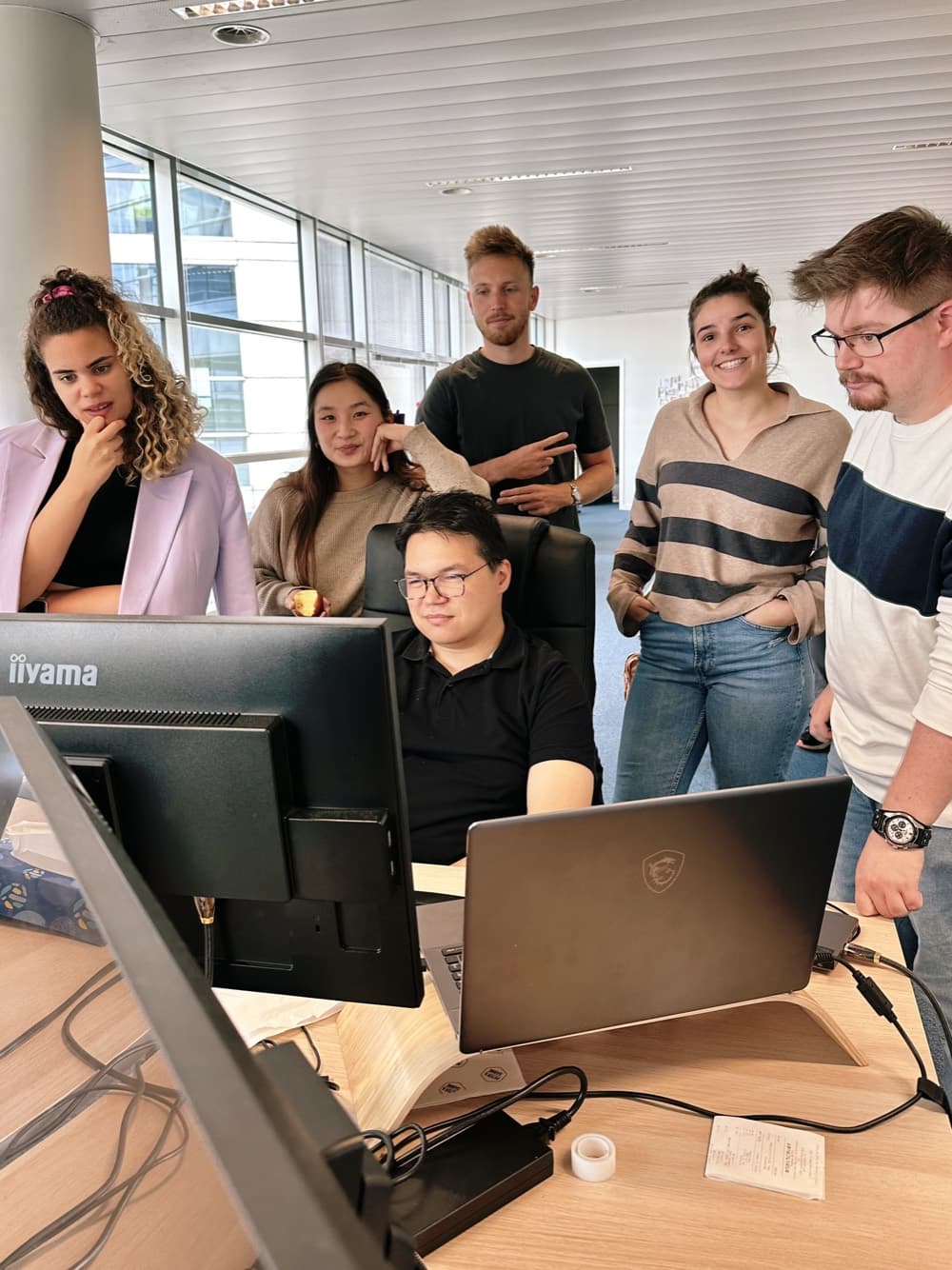 Five members of the Hilarious team gathered around a workstation, in the agency’s Brussels office.